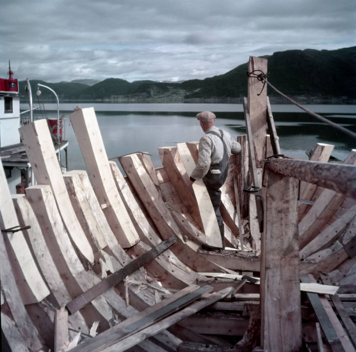 TREBÅTBYGGER: En trebåtbygger arbeider med bygging eller reparasjon av trebåter. Tidligere var det vanlig at fiskebåter ble bygget i tre. Her fra Rognan i 1953, kjent som stedet hvor fiskeskøyter bygges og repareres. Foto: Sverre A. Børretzen / Aktuell / NTB