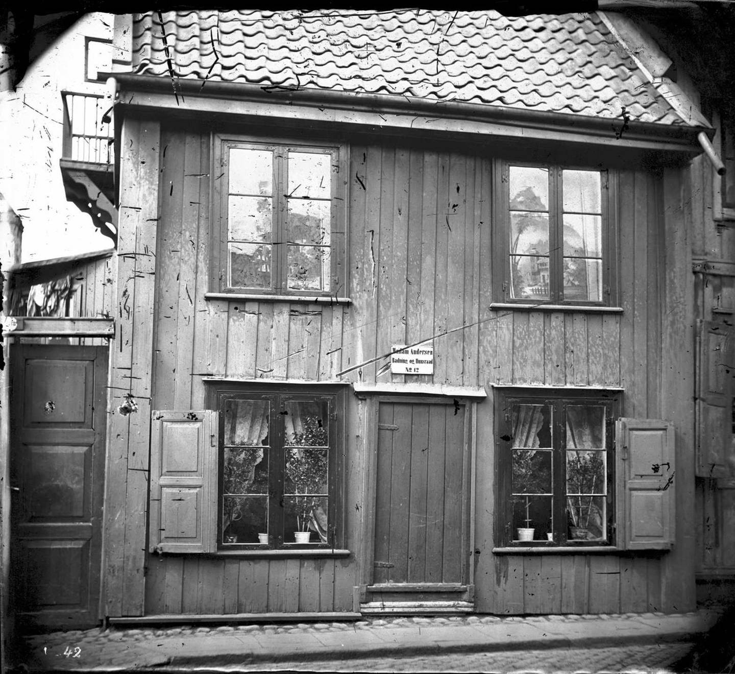 “Madam Andersen - Badning og Husraad” står det over døra. Huset ser innbydende og koselig ut, med dekorative rullegardiner og velsteltepotteplanter.