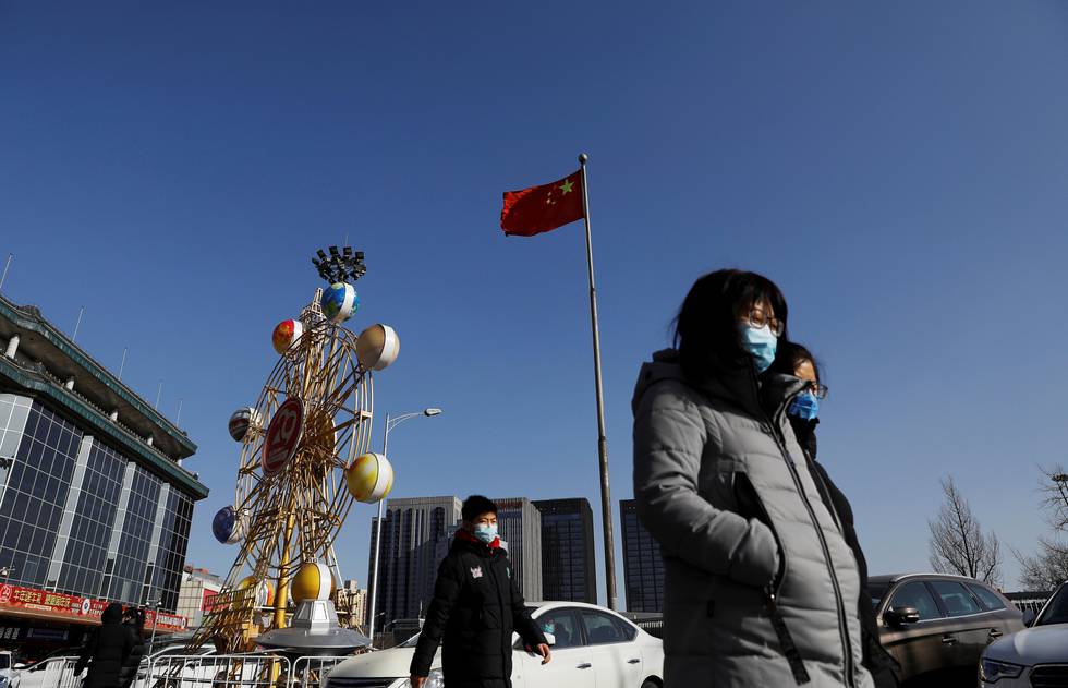 People wearing face masks walk past a Chinese flag, following new cases of the coronavirus disease (COVID-19) in the country, in Beijing, China January 11, 2021. REUTERS/Tingshu Wang