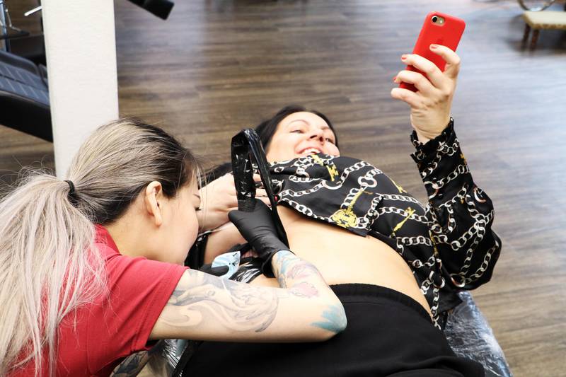 Evie Kristiansen fra Leap ink & piercing tatoverer, Veronica Simoné Fjeld oppdaterer snapchat med en mobil, mens en annen sender live på Instagram. Dermed skal seansen være grundig dokumentert. Foto: Lars Hjalmarsson