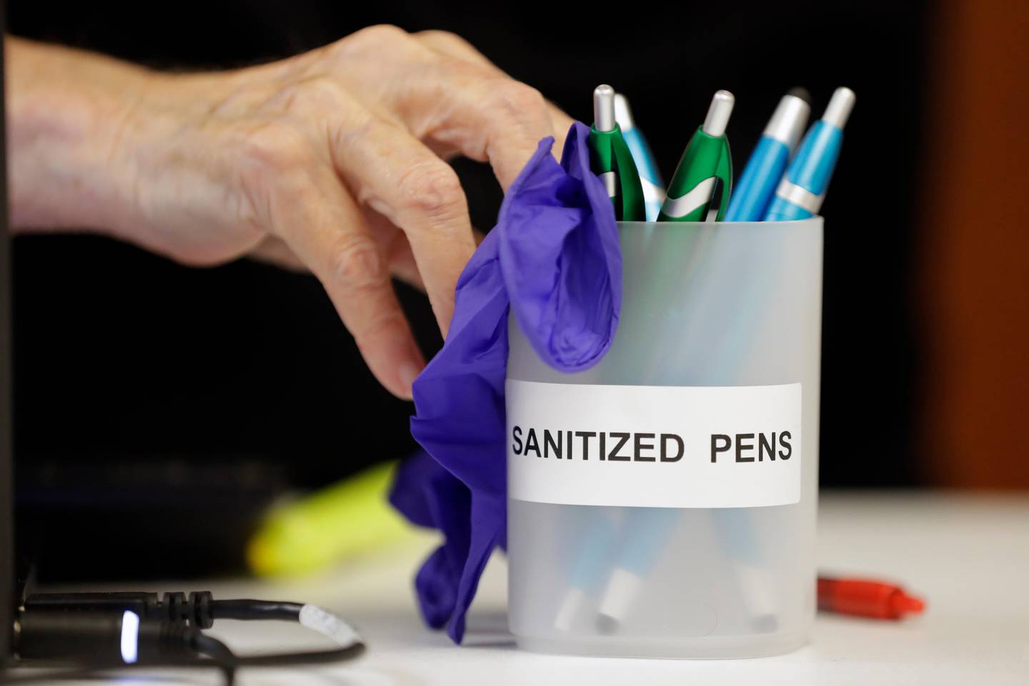 A poll worker pushes a container of sanitized pens to a voter to be used in voting Thursday, Aug. 6, 2020, in Brentwood, Tenn. The state is encouraging voters to wear masks and follow social distancing protocols at the polls. (AP Photo/Mark Humphrey)